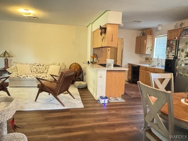 kitchen featuring light countertops, dark wood-type flooring, fridge with ice dispenser, a sink, and a peninsula