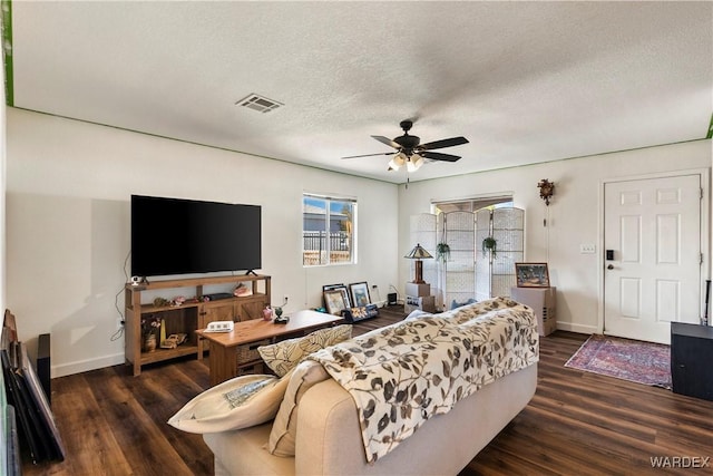 living area featuring dark wood finished floors, visible vents, ceiling fan, a textured ceiling, and baseboards