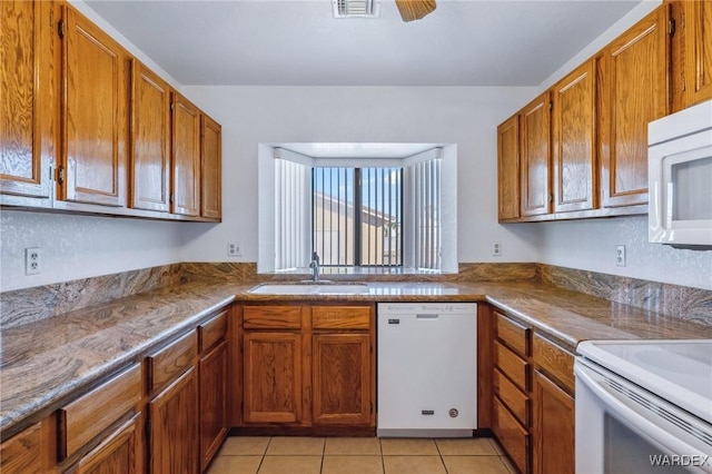 kitchen with white appliances, light tile patterned floors, brown cabinetry, ceiling fan, and a sink