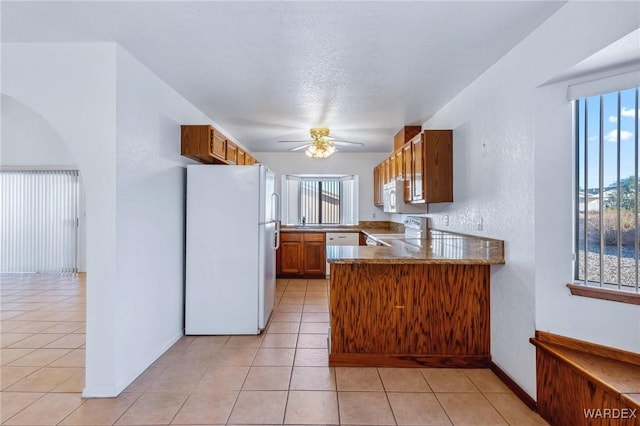 kitchen with a peninsula, white appliances, brown cabinets, and light tile patterned flooring