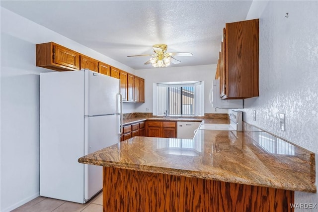 kitchen with light tile patterned floors, a peninsula, white appliances, a sink, and a ceiling fan