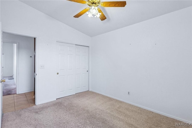 unfurnished bedroom featuring lofted ceiling, light tile patterned flooring, light carpet, baseboards, and a closet