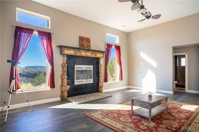 living room featuring a mountain view, dark wood-type flooring, a ceiling fan, baseboards, and a glass covered fireplace