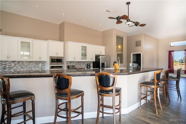 kitchen featuring stainless steel appliances, visible vents, a kitchen breakfast bar, white cabinetry, and glass insert cabinets