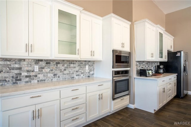 kitchen with white cabinets, light countertops, appliances with stainless steel finishes, dark wood finished floors, and glass insert cabinets