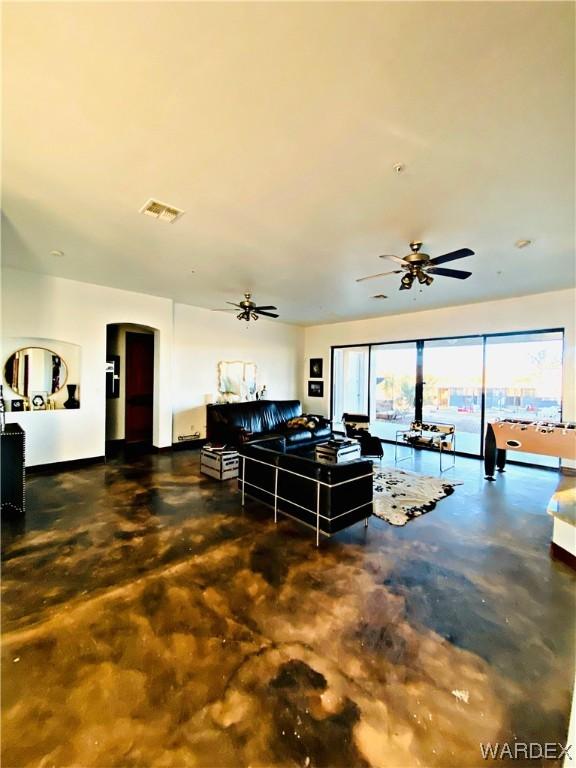 living area with arched walkways, visible vents, finished concrete flooring, and ceiling fan with notable chandelier