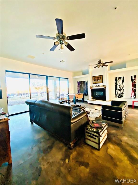 living room with concrete floors, a glass covered fireplace, and a ceiling fan