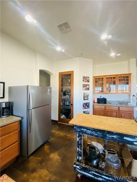 kitchen featuring visible vents, brown cabinetry, glass insert cabinets, freestanding refrigerator, and finished concrete floors