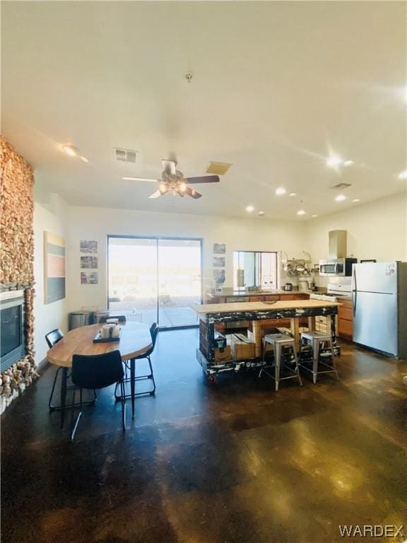 dining room featuring concrete flooring, visible vents, a stone fireplace, and a ceiling fan