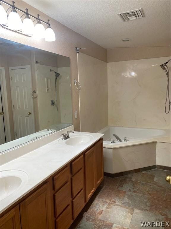 bathroom with double vanity, visible vents, a sink, a textured ceiling, and a bath