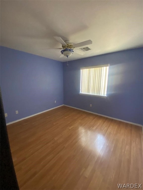 unfurnished room with a ceiling fan, wood finished floors, visible vents, and baseboards