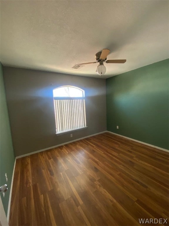 empty room with dark wood-style floors, a textured ceiling, a ceiling fan, and baseboards