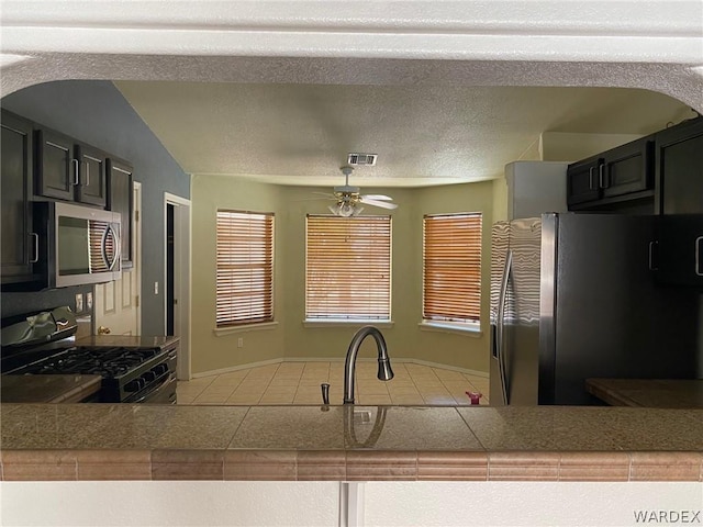 kitchen featuring a textured ceiling, stainless steel appliances, dark cabinetry, and visible vents