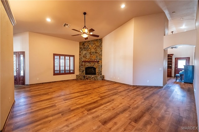 unfurnished living room with arched walkways, visible vents, a stone fireplace, and wood finished floors