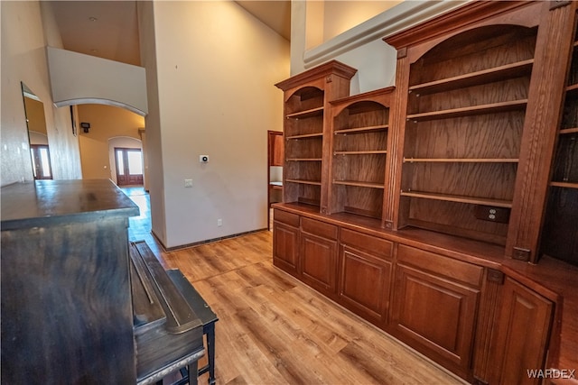 office featuring arched walkways, a high ceiling, baseboards, and light wood-style floors