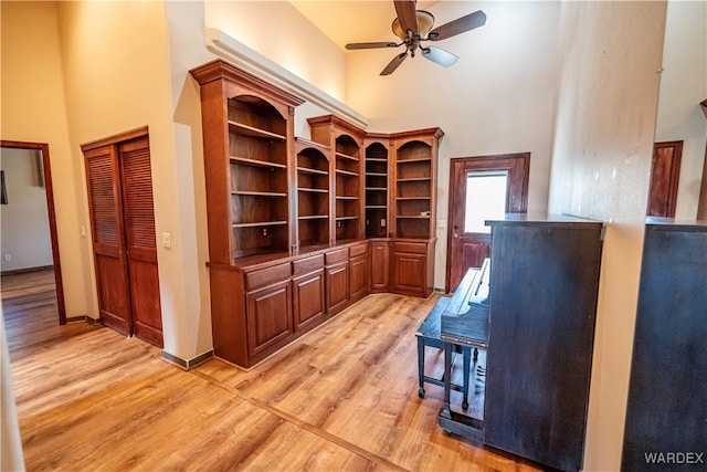 home office with a towering ceiling, light wood finished floors, baseboards, and a ceiling fan