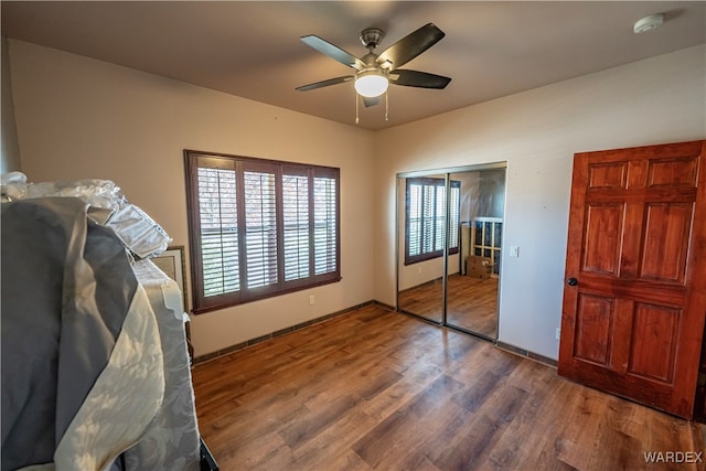 unfurnished bedroom with baseboards, a closet, a ceiling fan, and dark wood-type flooring