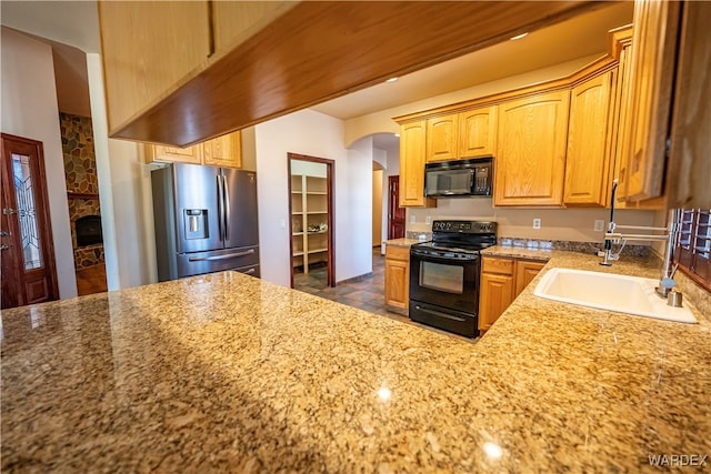 kitchen with light stone counters, arched walkways, a sink, a stone fireplace, and black appliances