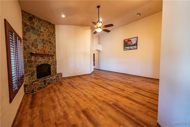 unfurnished living room with arched walkways, a fireplace, visible vents, a ceiling fan, and wood finished floors