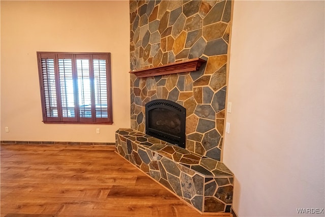 living room featuring baseboards, wood finished floors, and a stone fireplace