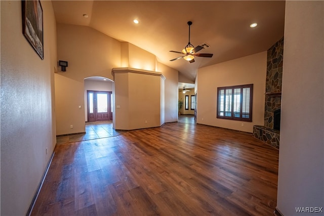 unfurnished living room with baseboards, arched walkways, ceiling fan, dark wood-type flooring, and a stone fireplace