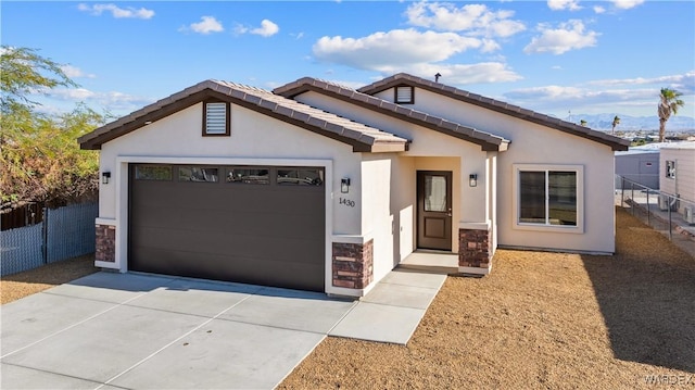 view of front of home with stucco siding, fence, a garage, stone siding, and driveway