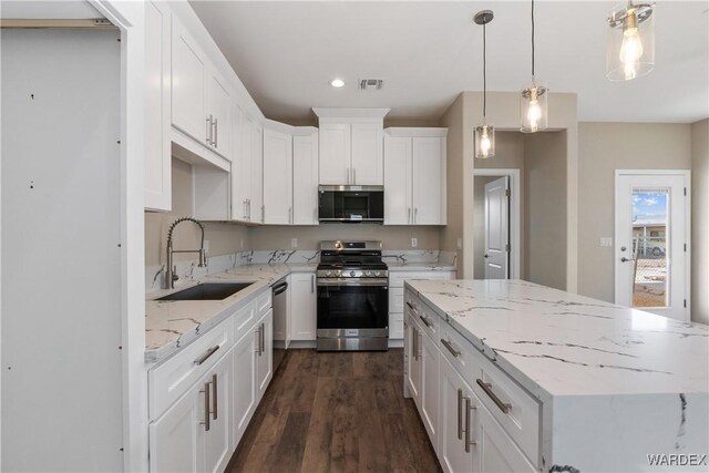 kitchen featuring decorative light fixtures, stainless steel appliances, white cabinets, a sink, and a kitchen island