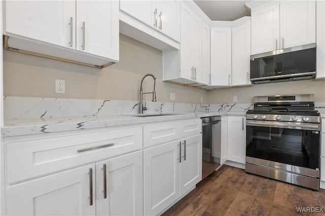 kitchen featuring stainless steel appliances, a sink, white cabinetry, light stone countertops, and dark wood-style floors