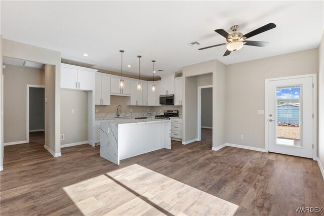 kitchen featuring a kitchen island, stainless steel microwave, white cabinets, and decorative light fixtures