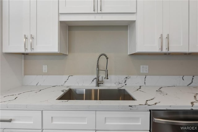 kitchen featuring stainless steel dishwasher, light stone counters, white cabinets, and a sink