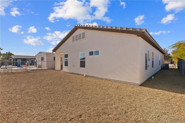 rear view of house with central air condition unit, fence, and stucco siding