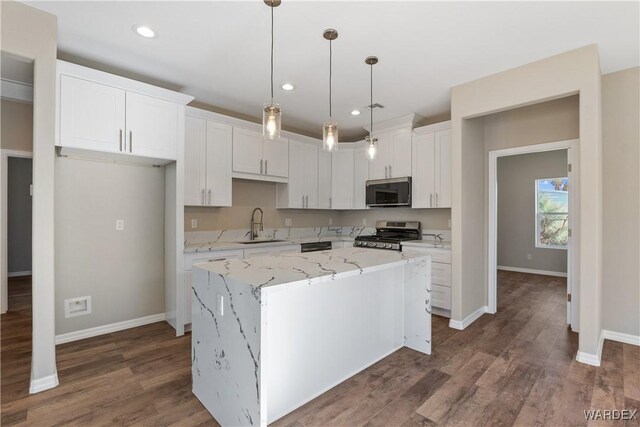 kitchen featuring appliances with stainless steel finishes, light stone counters, a center island, white cabinetry, and a sink