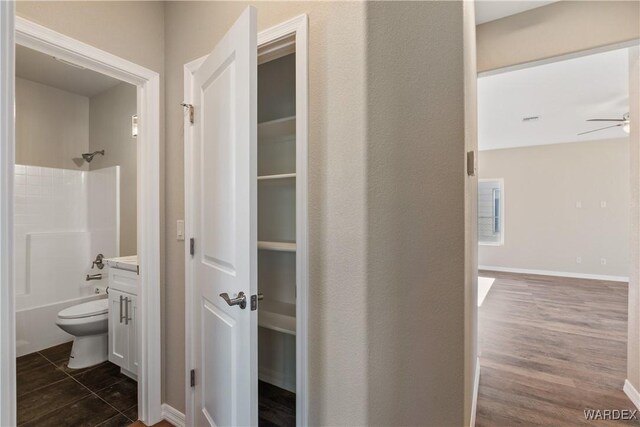 bathroom featuring baseboards, a ceiling fan, toilet, bathtub / shower combination, and vanity