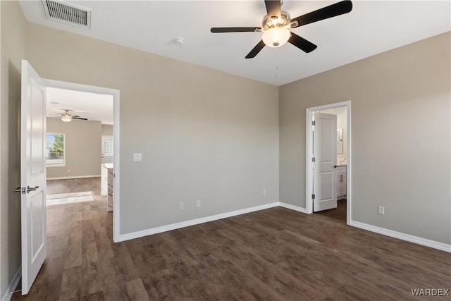 empty room featuring dark wood-type flooring, a ceiling fan, visible vents, and baseboards