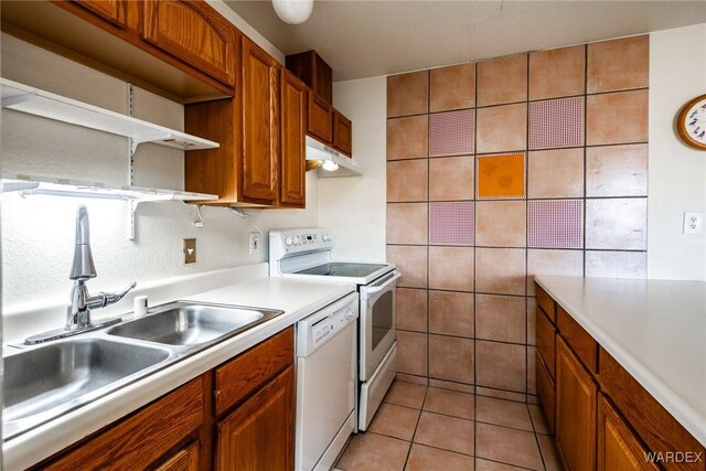 kitchen featuring light tile patterned flooring, white appliances, a sink, light countertops, and brown cabinetry