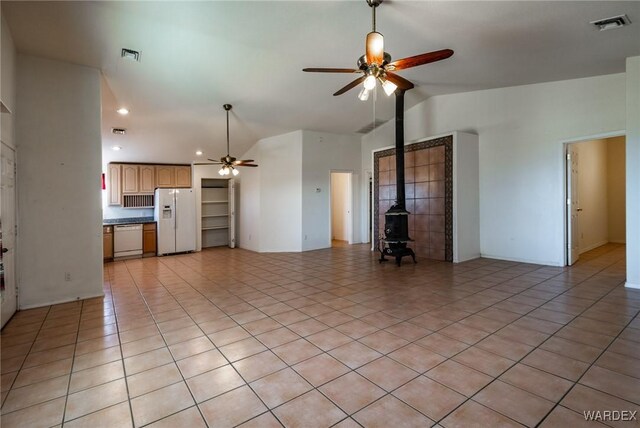 unfurnished living room featuring vaulted ceiling, visible vents, a wood stove, and a ceiling fan