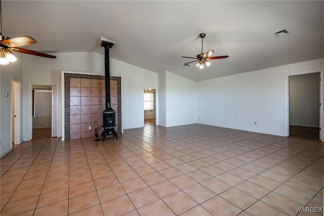 unfurnished living room with ceiling fan, lofted ceiling, light tile patterned flooring, visible vents, and a wood stove