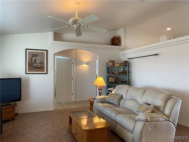 living area featuring lofted ceiling, arched walkways, a ceiling fan, and baseboards