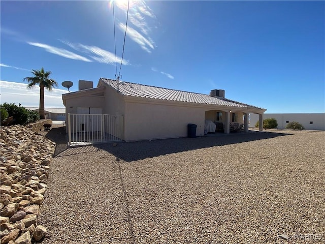 back of house featuring a tile roof, central AC, and stucco siding