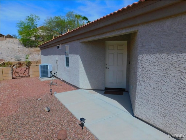 property entrance with central air condition unit, a tiled roof, fence, and stucco siding