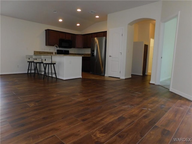 kitchen with stainless steel fridge with ice dispenser, arched walkways, dark brown cabinetry, dark wood-style floors, and black microwave