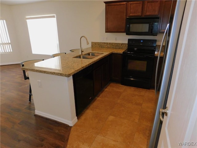 kitchen featuring a peninsula, black appliances, light stone countertops, a breakfast bar area, and a sink