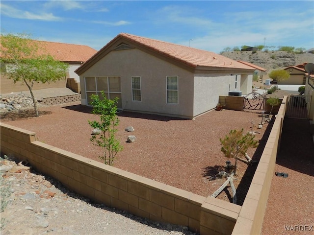 rear view of property featuring stucco siding, a tiled roof, and fence