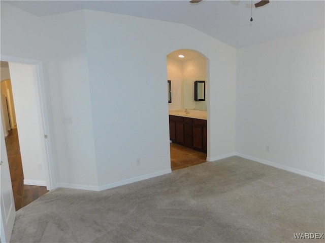 unfurnished room featuring baseboards, arched walkways, a ceiling fan, vaulted ceiling, and carpet flooring
