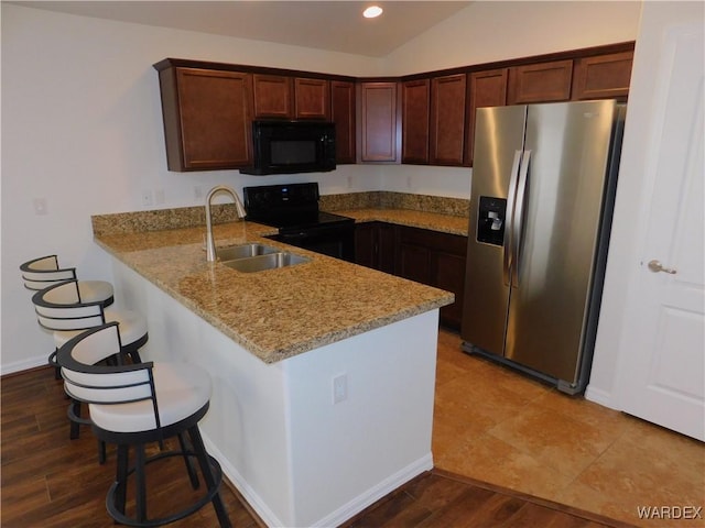 kitchen with light stone countertops, a kitchen bar, a peninsula, black appliances, and a sink