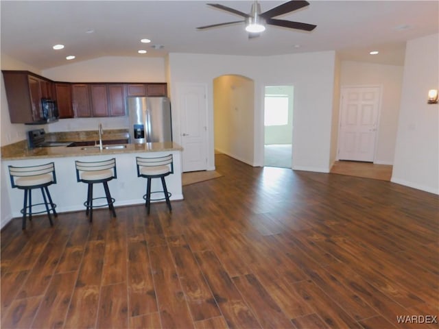 kitchen featuring a peninsula, a kitchen bar, appliances with stainless steel finishes, arched walkways, and a sink