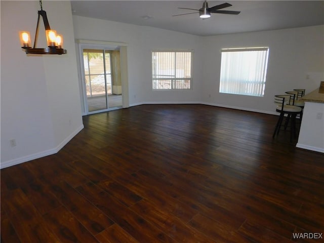 unfurnished room featuring ceiling fan with notable chandelier, baseboards, and dark wood-style floors