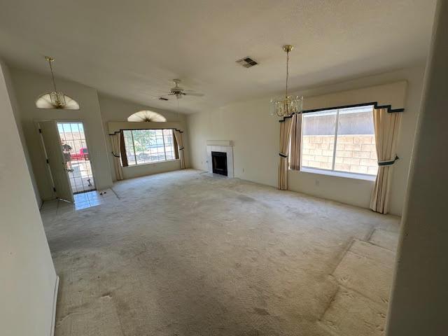 2195 Hijolly Dr, Bullhead City, AZ 86442 - unfurnished living room featuring light colored carpet, a fireplace, a chandelier, a ceiling fan, and vaulted ceiling