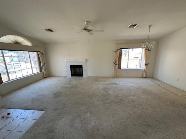 2195 Hijolly Dr, Bullhead City, AZ 86442 - unfurnished living room featuring a tiled fireplace, a chandelier, ceiling fan, and light carpet