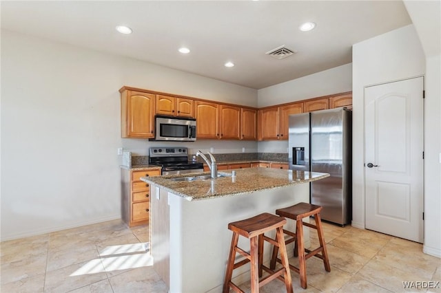 kitchen with visible vents, brown cabinets, a kitchen island with sink, stainless steel appliances, and a sink